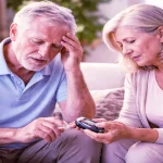 An elderly couple checking blood sugar with a glucometer to recognize signs of hypoglycemia at home.