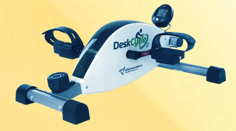 Close-up of the DeskCycle magnetic under-desk pedal exerciser with pedals and resistance knob shown under a desk.