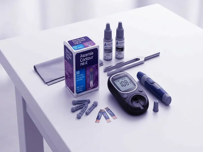 Ascensia Contour Next blood glucose meter displayed alongside test strips, lancing device, and control solution on a clean surface
